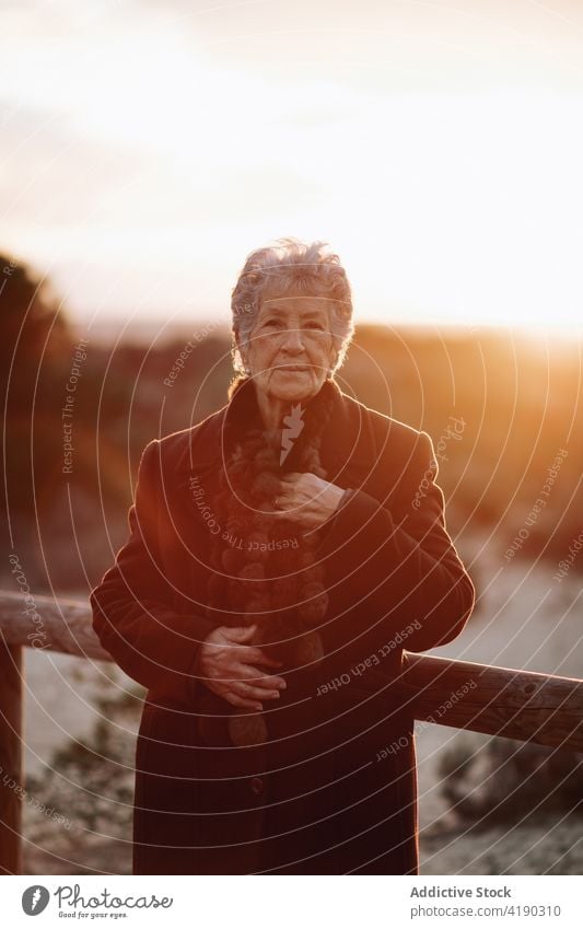 Senior lady admiring sunset over ocean from boardwalk woman admire seascape beach traveler enjoy nature vacation relax female elderly casual wooden pier