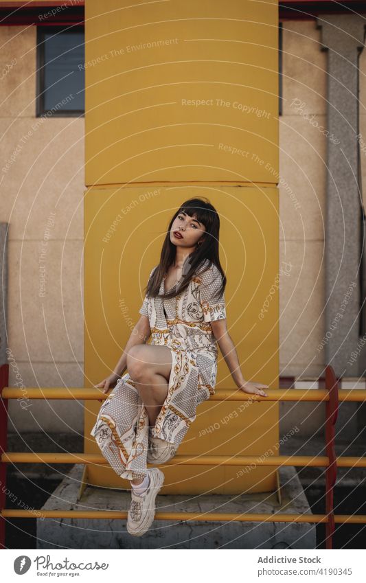 Trendy young ethnic woman resting on railing on street and looking at camera pensive trendy confident self esteem charismatic appearance fashion building female