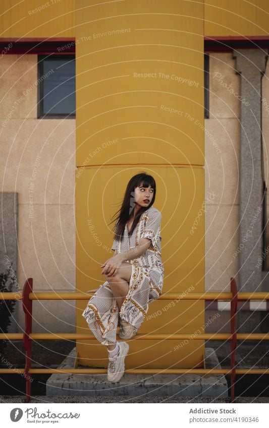 Trendy young ethnic woman resting on railing on street and looking away pensive trendy confident self esteem charismatic appearance fashion building female