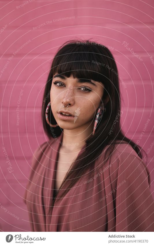 Fashionable young ethnic lady standing near pink wall and looking at camera woman pensive thoughtful style cool fashion calm street dreamy gorgeous brick wall