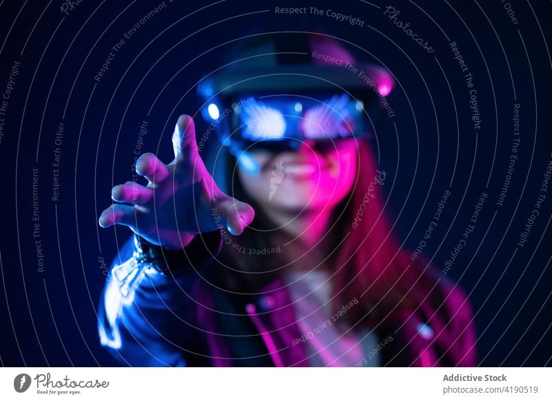 Anonymous woman in VR goggles in neon light vr headset outstretch virtual reality technology cyberspace illuminate simulate experience explore device projector