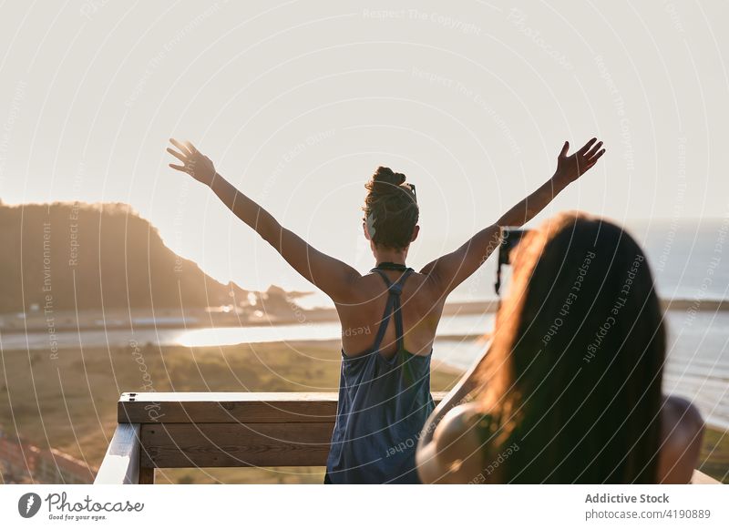 Woman taking photo of friend standing on balcony under seacoast women take photo sundown memory admire carefree freedom trip female together posture vacation