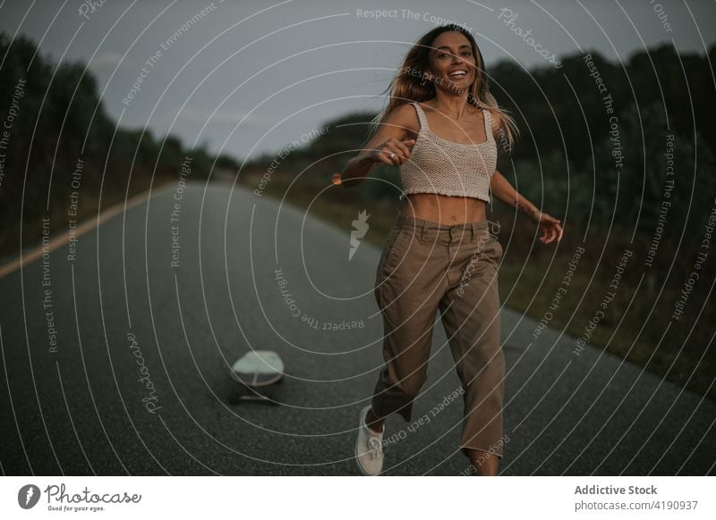 Joyful female skater running on empty rural road woman joyful carefree activity cruiser countryside twilight evening skateboard fit toothy smile casual