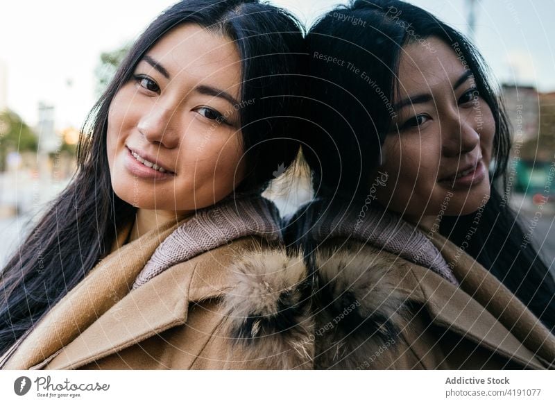 Charming ethnic female standing near glass wall woman reflection charming dreamy happy human face appearance individuality stare personality long hair street