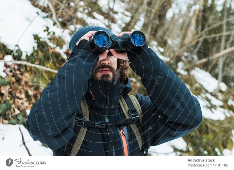 Traveling man looking in binoculars in winter forest traveler adventure hiker explore warm clothes male season snow nature woods vacation tourism cold frost