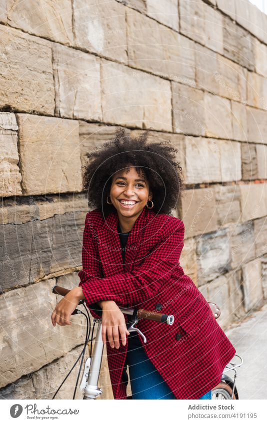 Delighted ethnic woman walking with bicycle in city street bike cheerful smile urban vehicle female black african american old stone wall building stroll enjoy