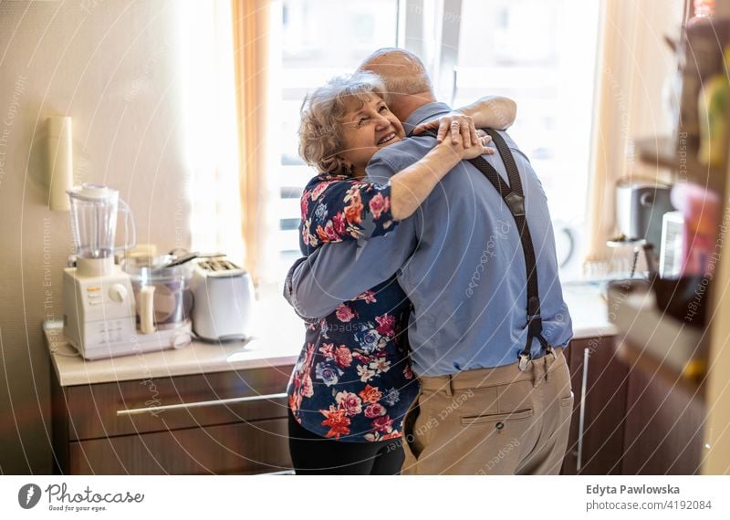 Elderly couple embracing and smiling in the kitchen real people candid genuine woman senior mature female together love bonding Caucasian elderly home house old