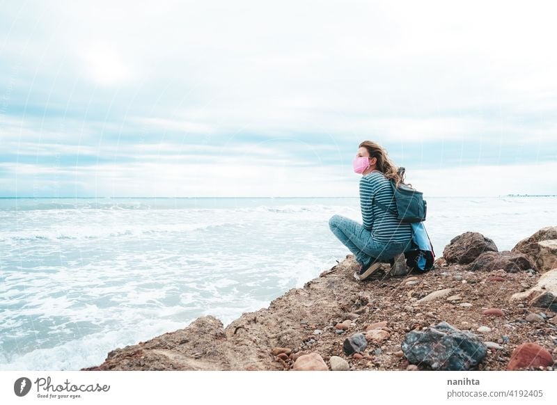 Young woman wearing a pink face mask sitting near the sea hope brave strong covid coronavirus beach ocecan free freedom survivor hopeful dream health medical