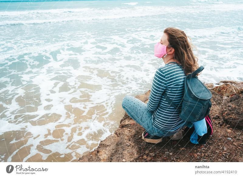 Young woman wearing a pink face mask sitting near the sea hope brave strong covid coronavirus beach ocecan free freedom survivor hopeful dream health medical