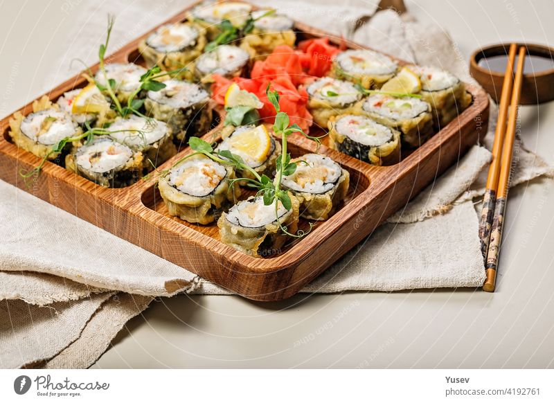 Hot rolls with eel, Japanese omelette, cream cheese, fried onions and unagi sauce, decorated with fresh herbs. Japanese food on a bamboo platter, bamboo sticks, sauce on a light background. Copy space