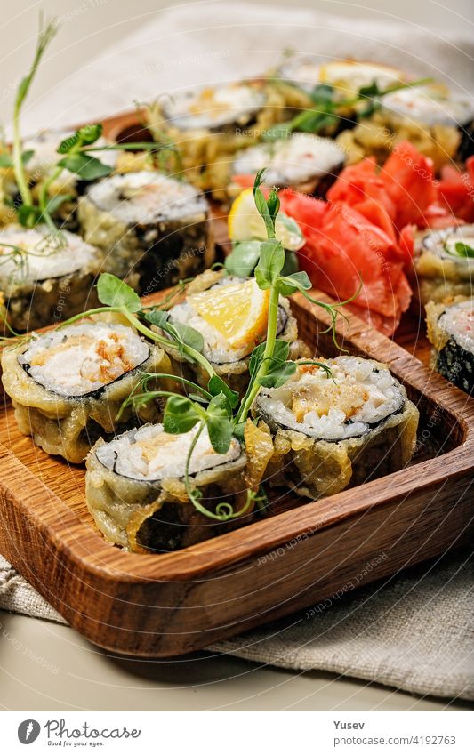 Close-up assorted hot rolls with eel, Japanese omelet, cream cheese, fried onions and unagi sauce with fresh herbs. Japanese food on a bamboo platter. Vertical shot