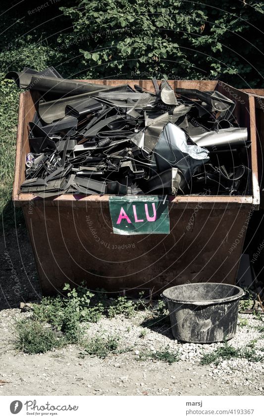 ALU. Well filled aluminium scrap container. Round mortar tub in the foreground. raw materials sustainable resources Sustainability Letters (alphabet) Lettering