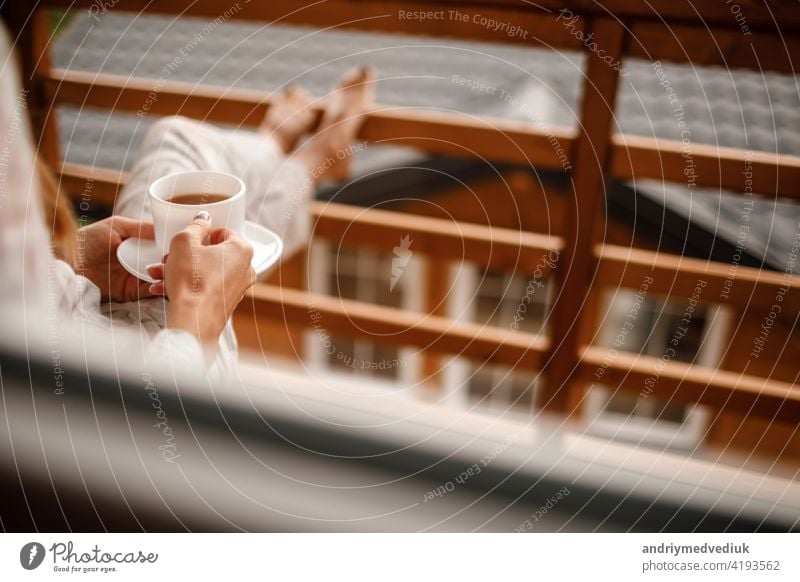 young woman in stylish nightwear enjoy drinking coffee or tea outdoor on balcony in the morning and looks at the mountains. girl holding cup hot summer relax