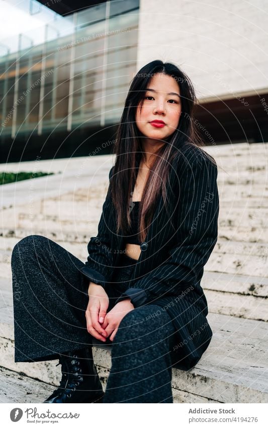 Long hair brunette asian woman sitting on some stairs and looking at camera japanese young female model chinese style attractive lady street modern stylish