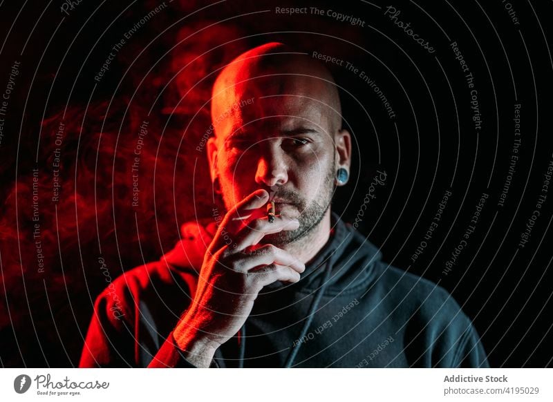 Male rocker smoking in dark studio smoke man cigarette brutal serious smoker tobacco male red light illuminate habit addict unhealthy personality style bald guy