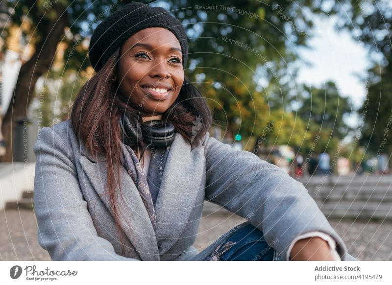 Serene ethnic woman relaxing in city street think thoughtful smile charming dreamy outerwear female black african american daydream casual carefree glad style