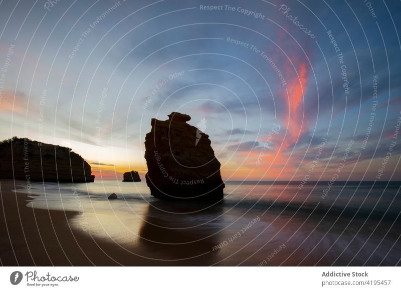 Rough rocks in blue ocean under sunste sky nature formation highland landscape seascape horizon blue sky cloudy geology Praia da Marinha Lagoa sunset majestic