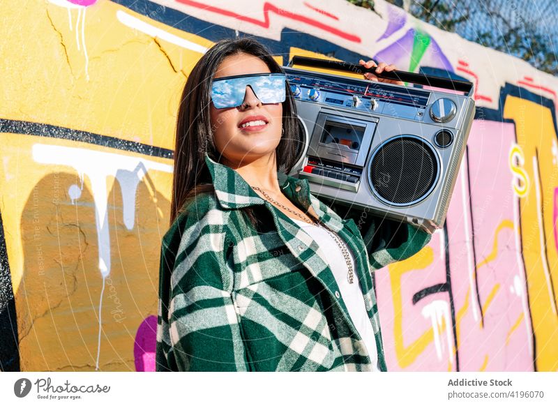 Stylish woman listening to music from retro cassette recorder outdoors fashion stylish graffiti town street art reflection cloudy sky device vintage tape