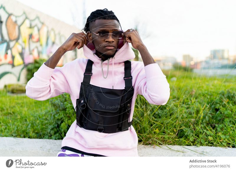 Serious black man sitting on concrete border in park confident put on cool hood trendy hipster individuality brutal style male masculine appearance thoughtful