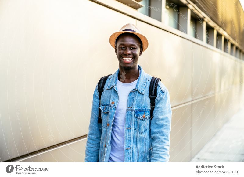 African-American man smiling near the wall cheerful sincere casual style friendly happy enjoy hand on hip denim jacket masculine bright modern cloth smile