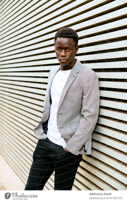 Stylish black man on urban pavement near ribbed wall stylish fashion masculine macho attentive model tiptoe town trendy apparel faded season style focus