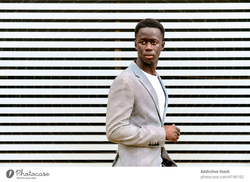 Stylish black man on urban pavement near ribbed wall stylish fashion masculine macho attentive model tiptoe town trendy apparel faded season style focus