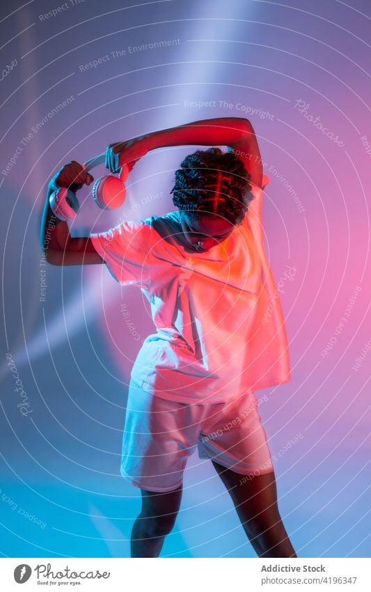 Black teen dancer in headphones in studio girl teenage light posture illuminate youngster neon cool glow generation urban bright modern confident style black