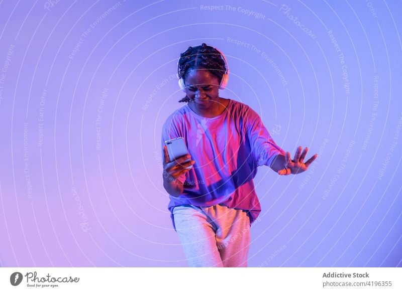 Black teen dancer with smartphone in headphones in studio girl teenage light posture illuminate youngster neon cool glow generation urban bright modern