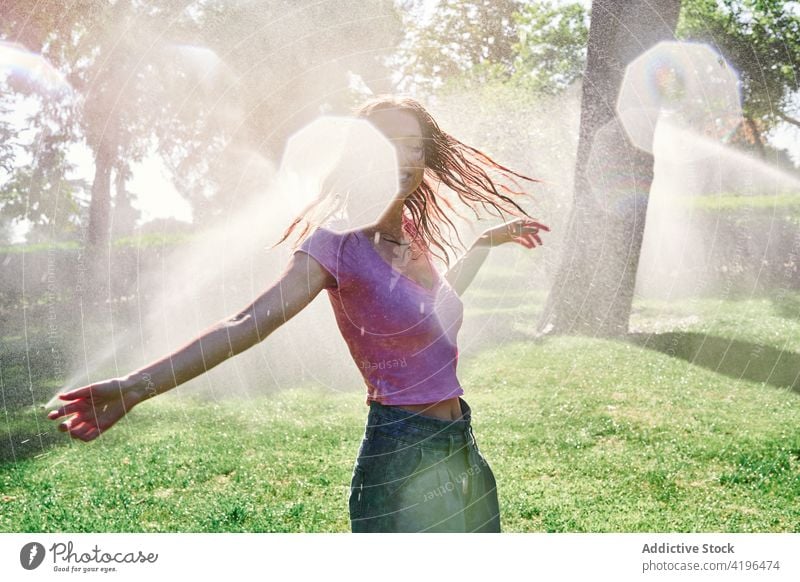 Happy teen woman standing under spray in park positive sunshine enjoy delight carefree splash expressive female nature teenage smile cheerful optimist sunny