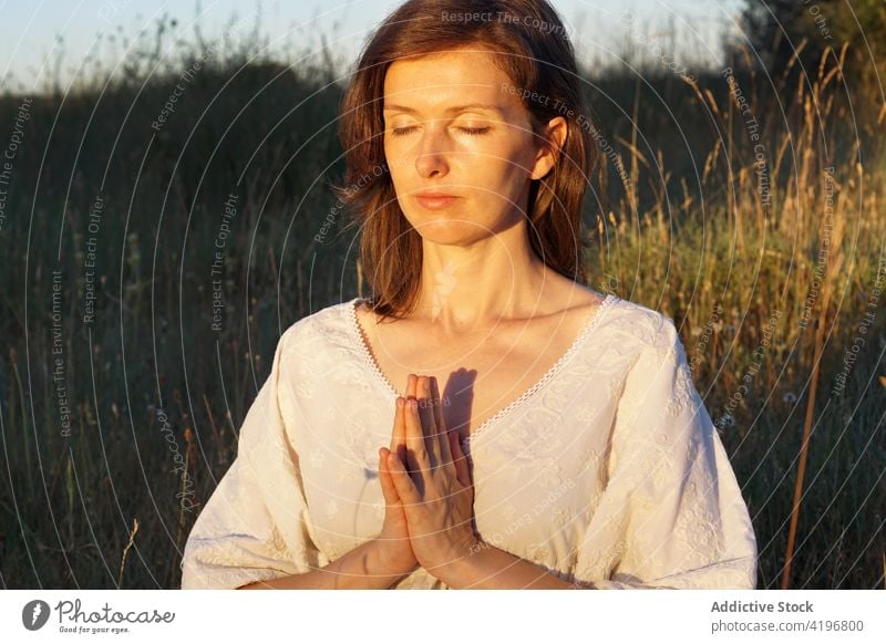 Tranquil woman meditating in field in summer meditate nature yoga practice tranquil mindfulness spirit female dress prayer gesture serene harmony peaceful