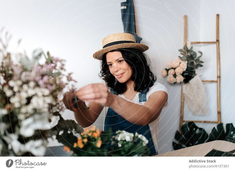 Gardener creating bouquet at table in house gardener plant foliage flower botany vegetate natural woman assorted tool trowel pot straw hat feminine