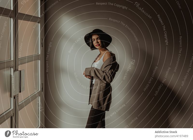 Stylish woman standing in room near window style outfit determine brutal trendy confident self assured female hat jacket appearance personality fashion serious