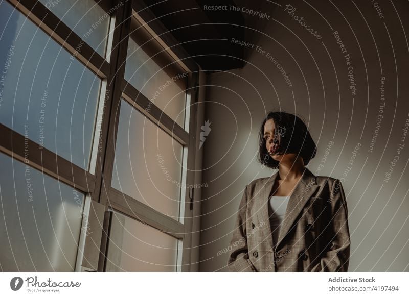 Stylish woman standing in room near window style outfit determine brutal trendy confident self assured female hat jacket appearance personality fashion serious