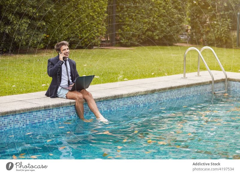 Businessman dressed in a suit sitting on the edge of the pool with a laptop work person businessman swimming computer phone talking speaking internet people