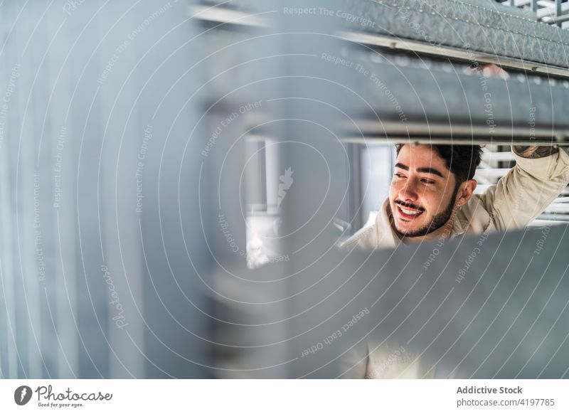 Crop smiling ethnic man behind metal construction in town content admire masculine macho brutal hipster enjoy hole cheerful friendly urban smile casual sincere