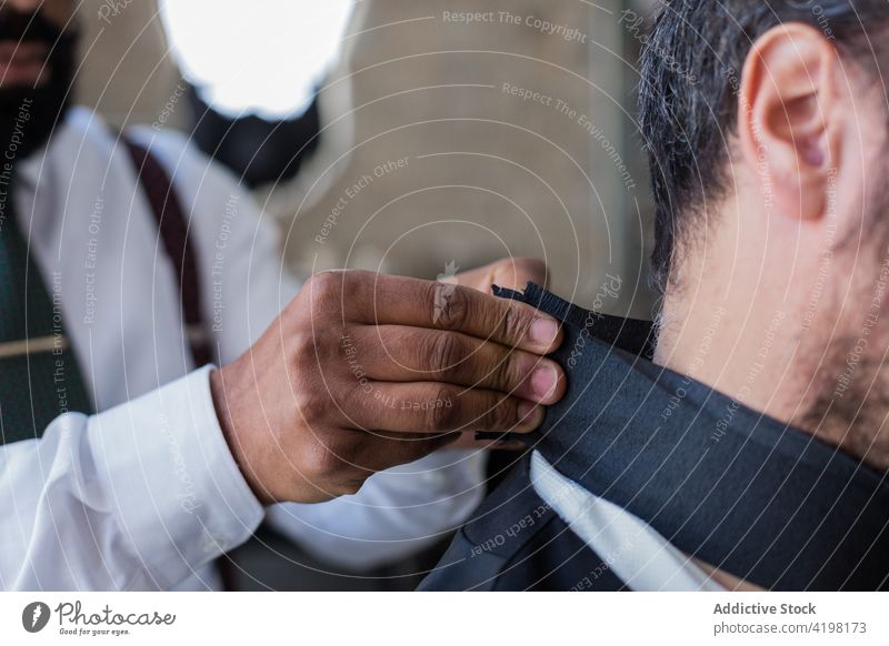 Ethnic stylist with hipster client preparing for procedure in barbershop hairstylist prepare profession masculine stylish men formal tie process together