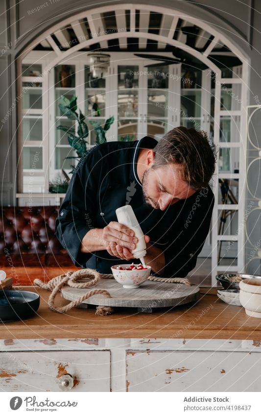 Focused man decorating dessert with cream in stylish restaurant decorate chef berry delicious cook concentrate job culinary prepare male young beard uniform