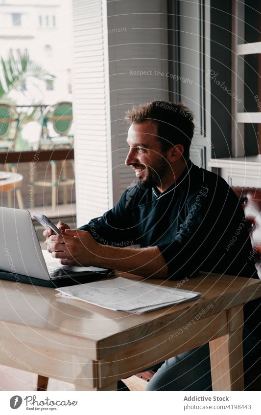 Cheerful businessman using smartphone and laptop for work chef cheerful entrepreneur surfing connection male cellphone smile happy occupation job online beard