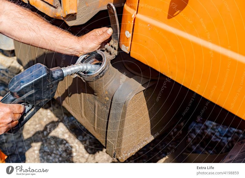 Hand holding handle fuel nozzle to refuel, petrol is pouring into the tank of an industrial mechanization Activity Barrel Building Site Bulldozer