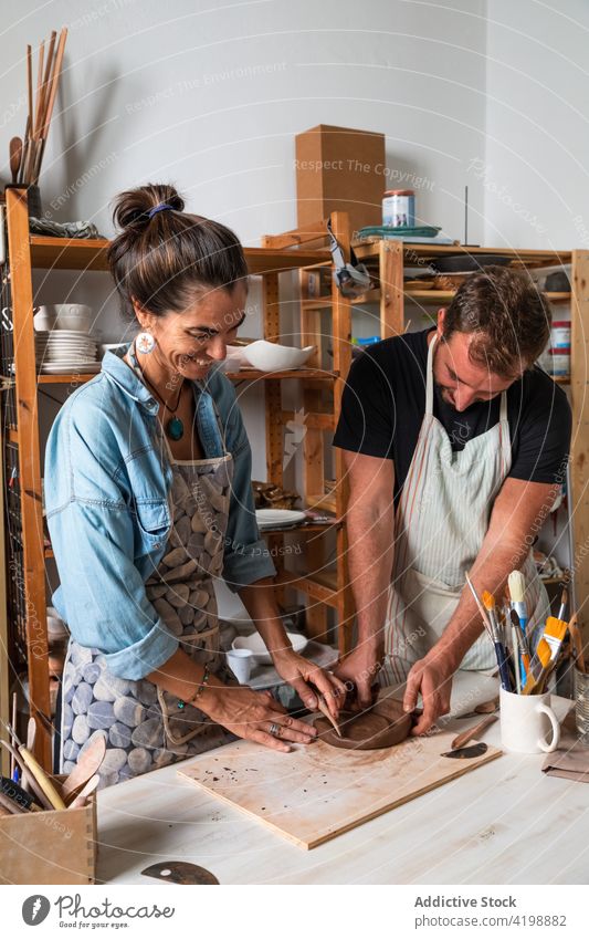 Happy coworkers sculpting clay plate in workshop colleague create clayware smile positive class hobby together skill help man woman middle age young diverse