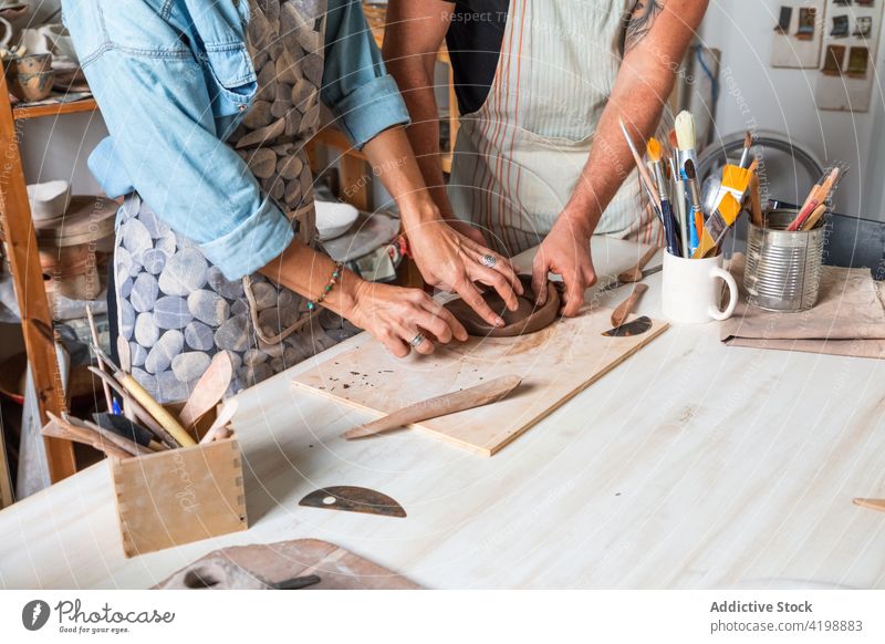 Anonymous coworkers sculpting clay plate in workshop colleague create clayware smile positive class hobby together skill help man woman casual apron pottery