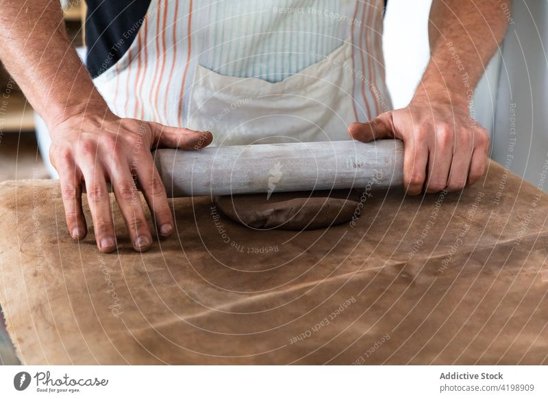 Anonymous man kneading clay while creating tableware in workshop roll up clayware create rolling pin job handicraft pottery skill male apron master