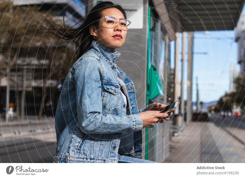 Long hair brunette Asian woman using mobile phone while sitting on a bench in the street cellphone asian chinese female japanese smartphone girl happy people