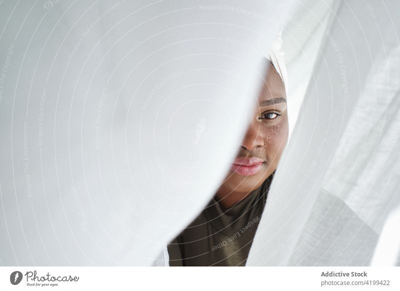 Smiling black lady behind curtains and looking at camera woman smile positive feminine hide grace calm charismatic style glad joy female young african ethnic