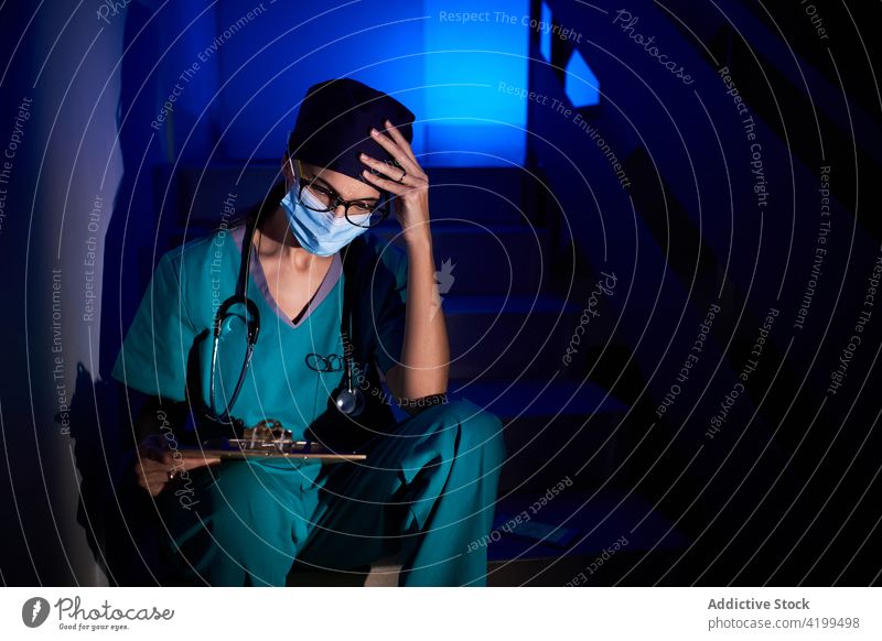 Thoughtful doctor reading documents in darkness thoughtful woman examine medical report pensive female clinic stair staircase stairway step blue neon light