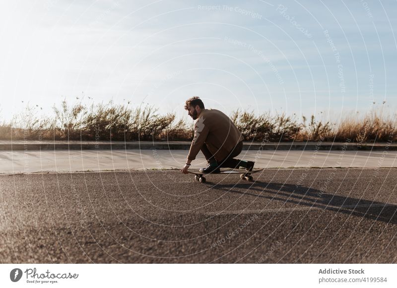 Trendy skater performing trick on rural road man countryside nature asphalt touch ground skill talent male ride activity energy motion skateboard hobby move