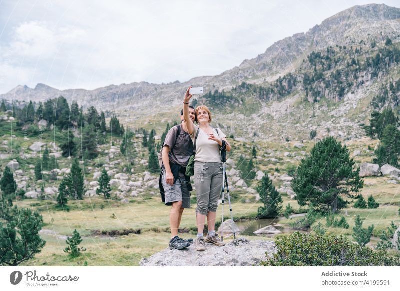 Couple of hikers taking selfie on smartphone against mountain memory moment highland nature couple using gadget self portrait device tree cloudy sky trekker