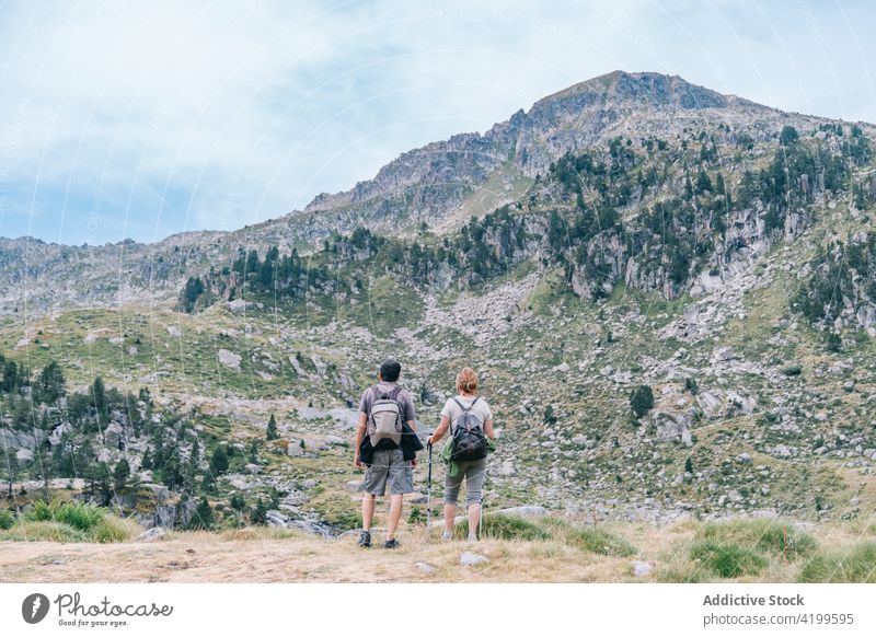 Unrecognizable couple of hikers trekking on mountains landscapes stroll path vacation route nature trip pole summer together partner rough pathway travel