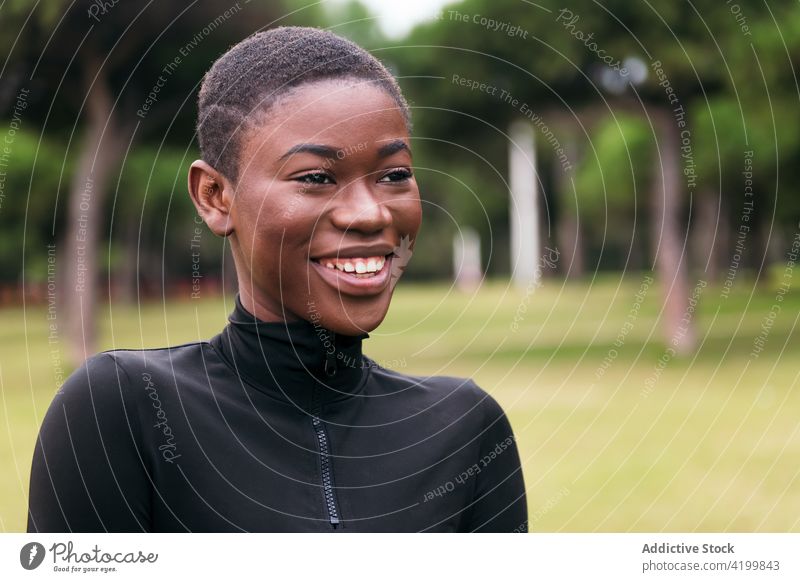 Gentle black woman in casual wear in city park feminine gentle short hair tender sincere friendly charming pleasant portrait urban lawn body belly harmony style