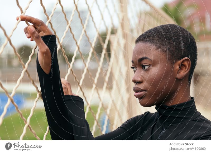 Melancholic black woman near grid fence in town short hair melancholy wistful reflective feminine solitude gentle urban portrait style city apparel casual